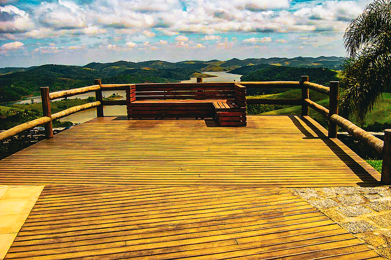 Deck de madeira com guarda-corpo roliço voltado para represa e montanhas
